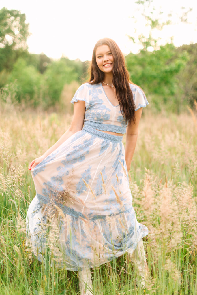 Senior girl standing in tall golden grass in Yorktown, wearing a stylish blue dress with soft golden-hour light.