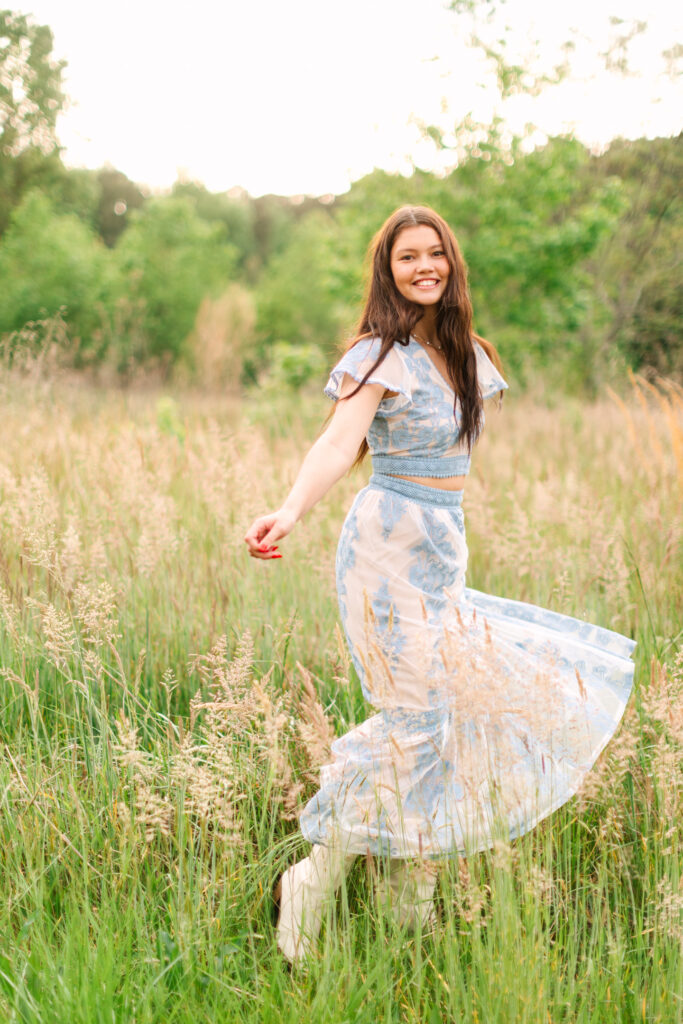 Senior twirling in an open field in Yorktown with golden light catching her blue dress and movement.