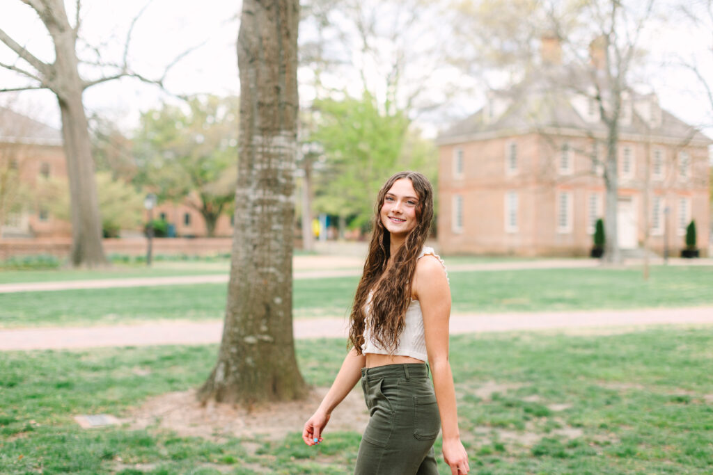 Senior walking through the College of William & Mary campus in Williamsburg with historic brick buildings and warm afternoon light.