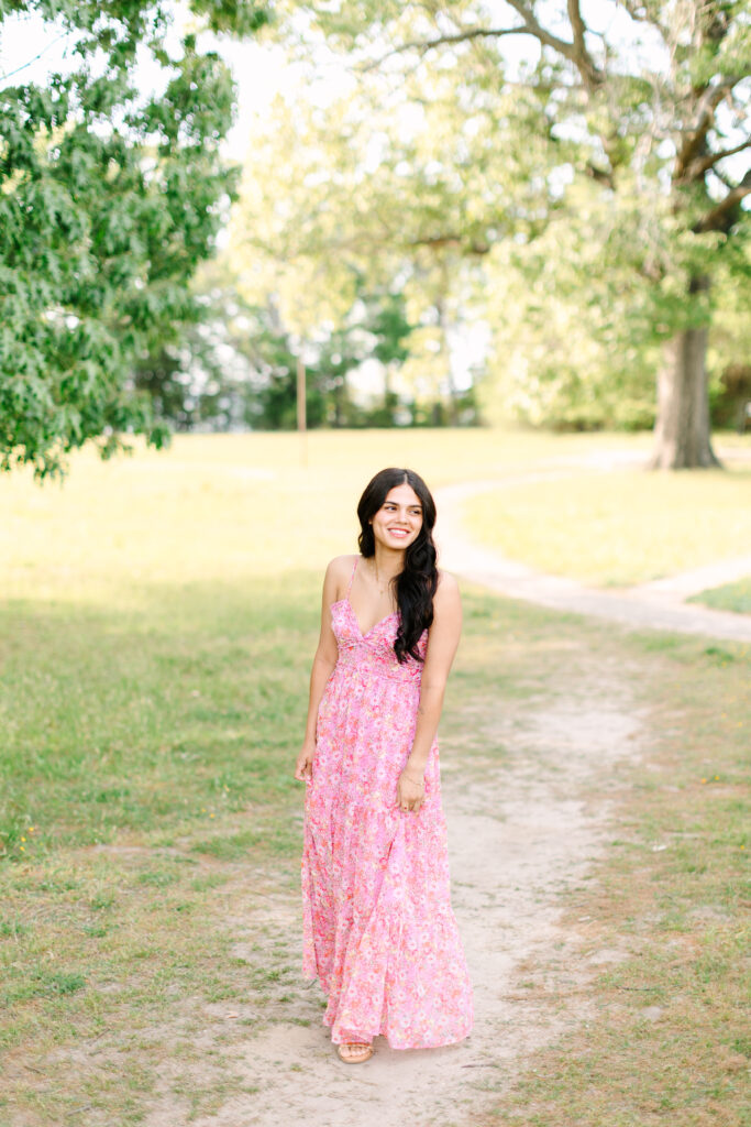 Senior portraits in Yorktown walking along a wooded trail, surrounded by trees and soft sunlight.
