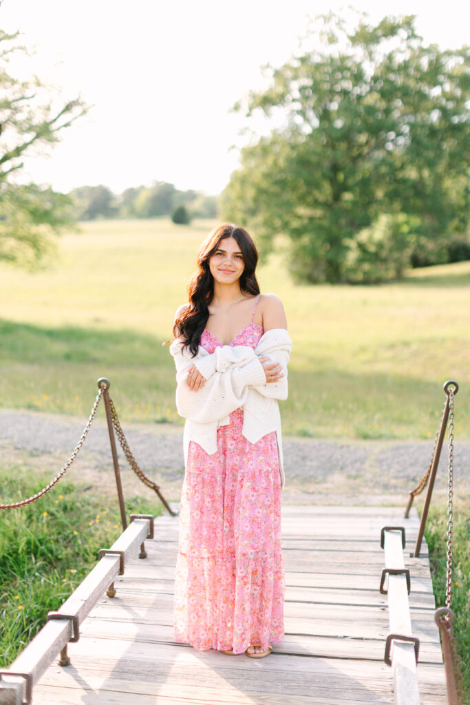 Senior girl standing on a wooden footbridge in Yorktown, surrounded by trees and warm evening light.