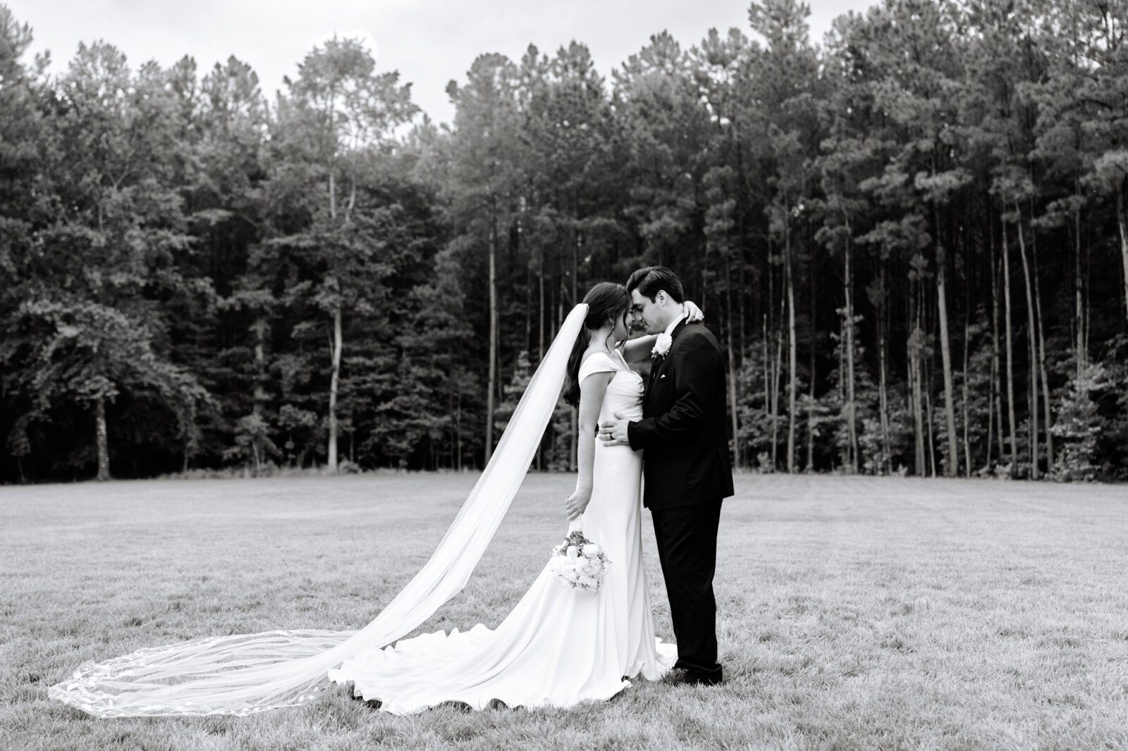 Black and white wedding portrait of the bride and groom with trees in the background at The Maine of Williamsburg