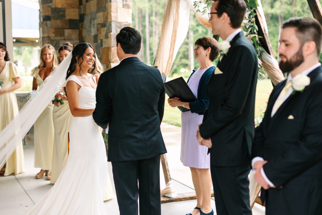 Bride smiling at the groom during the wedding ceremony at The Maine of Williamsburg