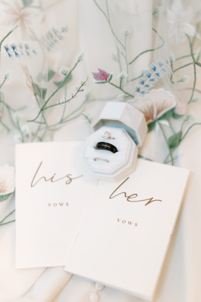 Bridal veil with colorful embroidered flowers, vow books, and rings during a wedding at The Maine of Williamsburg