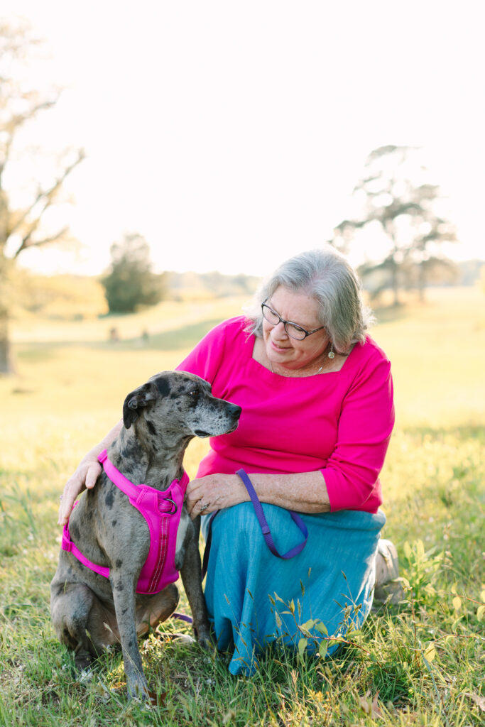 Woman in pink posing with her dog in a matching pink harness during a golden hour summer mini session in Yorktown, Virginia.